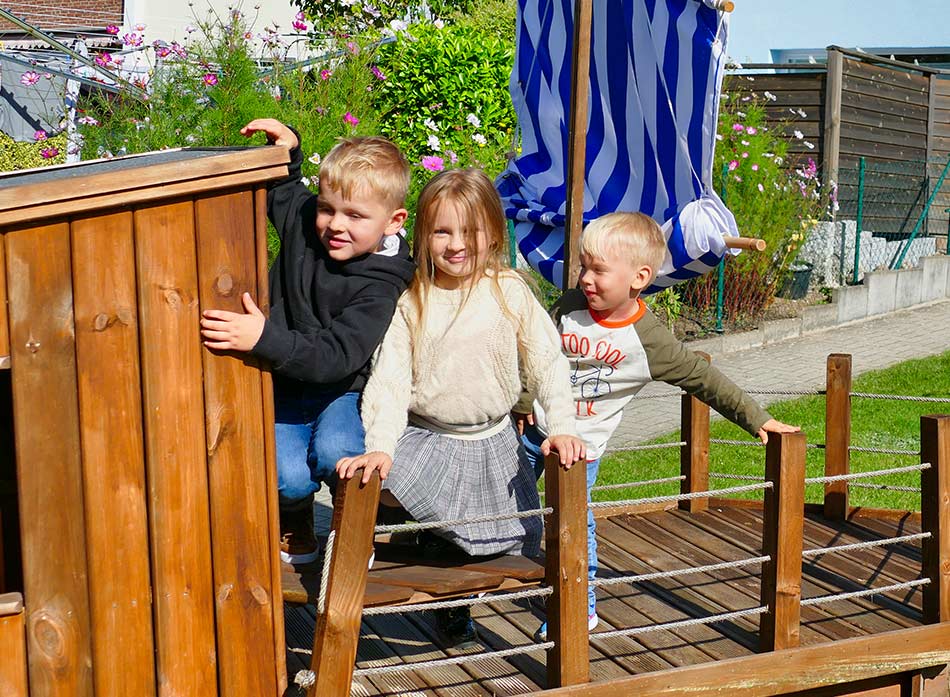 Drei Kinder klettern auf dem Piratenschiff im Garten